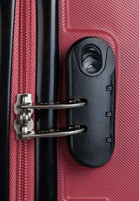 Maleta roja con un exterior texturizado, detalles de cremallera, herrajes metálicos y un mecanismo de bloqueo negro con acentos estriados.