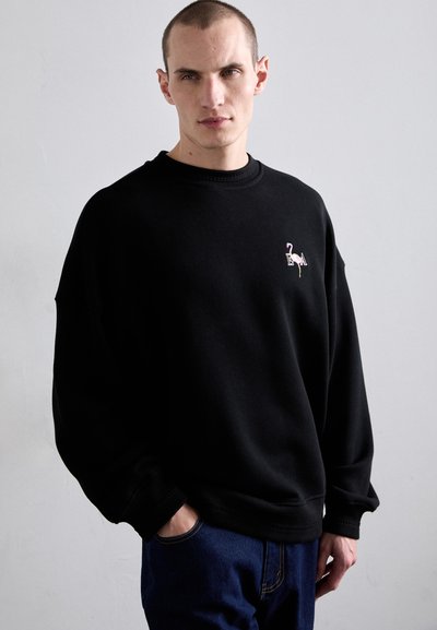 Sort sweatshirt lavet af bomuld, med rund hals og drop skuldre. Inkluderer en lille, farverig flamingo broderi på brystet.