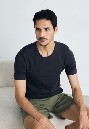 Herrliches T-Shirt aus dunkelgrauer Baumwolle, Kurzarm, runder Halsausschnitt, mit subtiler Marken-Logo. Dazu leichte grüne Shorts.