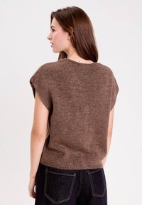 Pull en tricot marron à manches courtes, col rond et finition texturée. Associé à un jean foncé avec poches arrière.