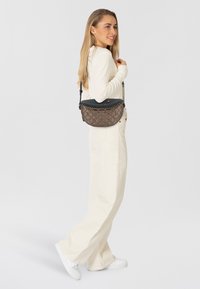 Borsa a tracolla marrone trapuntata con parte superiore nera, dotata di una tracolla a catena. La borsa ha una forma curva e una texture liscia, completata da un corpo decorato.