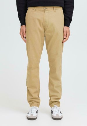 Khaki chinos with a smooth cotton fabric, straight-leg design, belt loops, and a single button closure, paired with white sneakers.