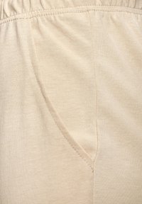 Beige fabric with a smooth texture, featuring a side pocket and an elastic waistband. The stitching is visible along the edges.