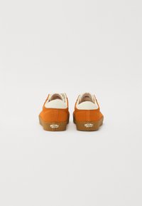 Orange suede sneakers with a white heel cap and brown rubber sole. Features logo plate on the back and minimal stitching detail.