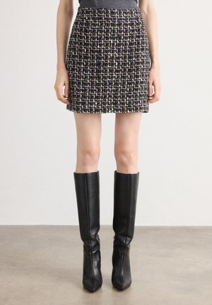 Tweed skjørt i svart, lilla og gul, med en tettsittende design og teksturert stoff, kombinert med høye svarte skinnstøvler.
