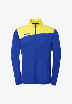 Blauw sportjack met een geel schouderstuk met geometrisch patroon, volledige ritssluiting aan de voorkant en Kempa-logo op de linkerborst.