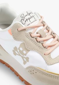 Zapatilla blanca con detalles en ante beige, cordones rosas y un logo de calavera y huesos cruzados. Presenta una suela texturizada y un diseño cosido.