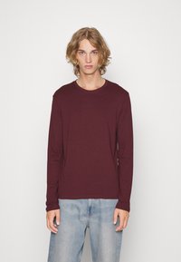 Bordeaux langærmet T-shirt lavet af blødt stof, med rund halslinje og tætsiddende ærmer, parret med lyseblå afslappede jeans.