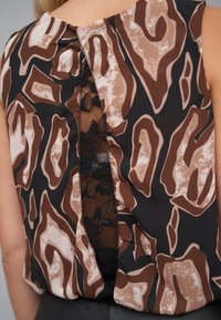 Brązowo-czarny wzorzysty top z koronkowym tyłem, z wstawką z kwiatowej koronki i gładką fakturą materiału. Okrągły dekolt.