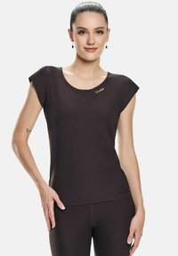 Tricou cu mânecă scurtă, de culoare maro închis, cu decolteu rotund, având un logo aurit pe umărul stâng. Textură netedă și design ajustat.