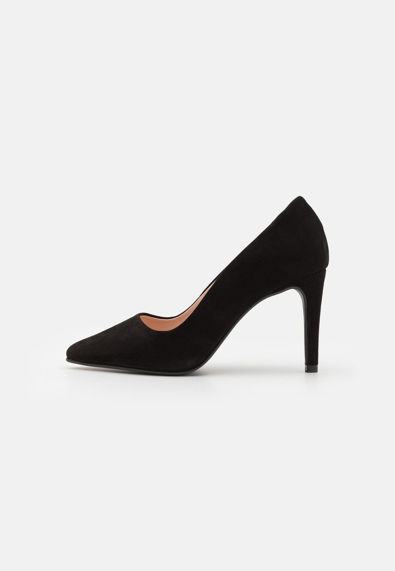 Escarpin en daim noir avec un bout pointu et un talon aigu haut. Il présente une découpe incurvée sur les côtés pour un design épuré.
