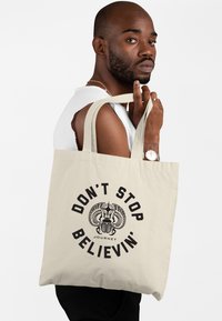 Canvas tote bag i ljusbeige, med svart text och en grafisk design med en skalbagge och horn. Robust, med två axelremmar.