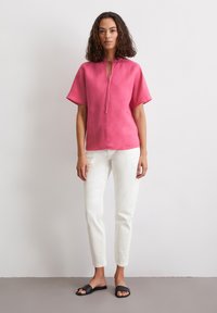 Helles pinkes Leinenoberteil mit weiten Ärmeln und einer Halsbandage, kombiniert mit weißen schmalen Hosen und schwarzen Rutschschuhsandalen, minimalistischem Design.