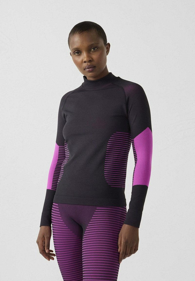 Camiseta deportiva de manga larga en negro con acentos de rayas moradas en las mangas y los costados, hecha de un material elástico y texturizado.