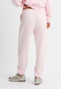 Helle rosa Sweatpants mit elastischem Bund und gerippten Knöcheln, kombiniert mit silbernen und grauen Sportschuhen. Weicher, glatter Stoff.