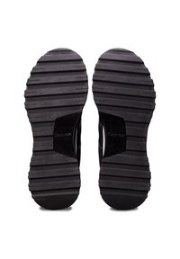 Semelles de chaussures en caoutchouc noir avec des rainures horizontales et le logo « Calvin Klein » au centre de chaque semelle.