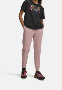 Černé tričko s krátkým rukávem s květinovým motivem, zkombinované s růžovými zúženými tepláky a vícebarevnými sportovními botami.