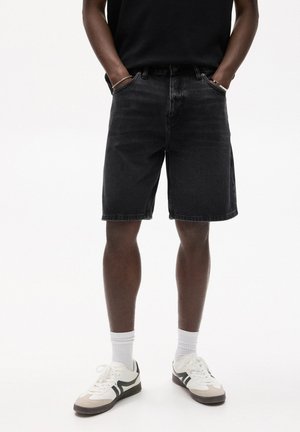 Zwarte denim short met een rechte snit, voorzien van voorzakken en een klassieke tailleband. Gepaard met witte sportschoenen en korte sokken.