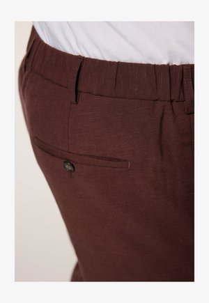 Pantalones de tela marrón texturizada con cintura elástica y un bolsillo trasero con cierre a presión negro.