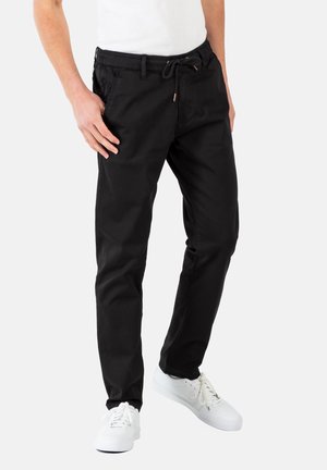 Schwarze Jogginghosen aus weichem Stoff mit elastischem Bund und Kordelzug, seitlichen Taschen und schmal zulaufenden Beinen. Getragen mit weißen Turnschuhen.