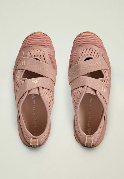 Light pink athletic shoes with mesh upper, elastic straps, and rubber sole. Features branding on straps and insole.