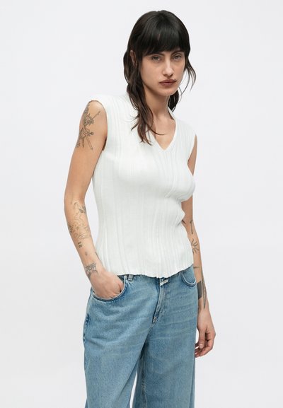 Λευκό ριμπ αμάνικο τοπ με V-λαιμόκοψη και κυματιστό τελείωμα, συνδυασμένο με ανοιχτό μπλε distressed τζιν παντελόνα με φαρδιά πόδια.