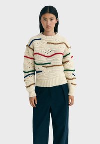 Flauschiger, creamfarbener Strickpullover mit mehrfarbigen, wellenförmigen Streifen in Rot, Blau, Grün und Braun, einem strukturierten Muster und gerippten Bündchen.