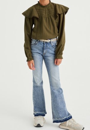 Oliwkowa bluzka z falbankami na rękawach i pionowymi szwami, zestawiona z jasnoniebieskimi, rozszerzanymi dżinsami z postrzępionymi końcami i białym paskiem.