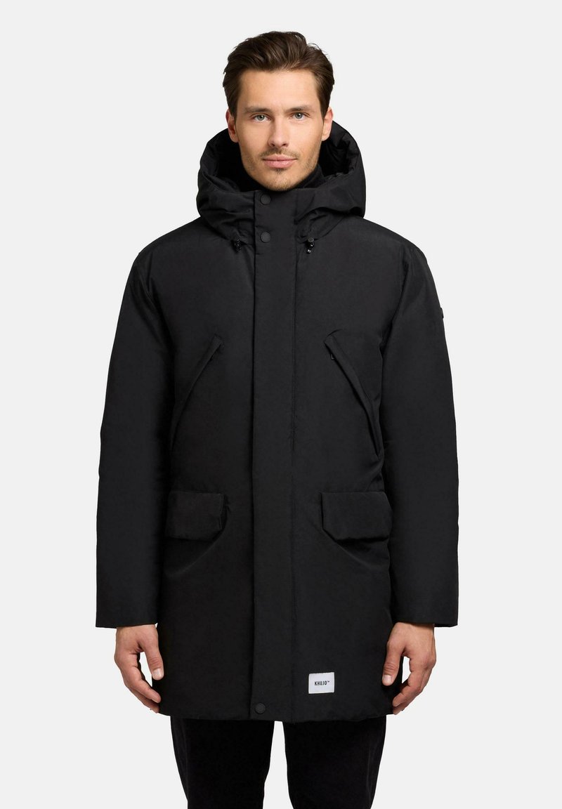 Black puffer coat with a hood, featuring a straight cut, front snap closure, two large patch pockets, and branded label on the bottom.