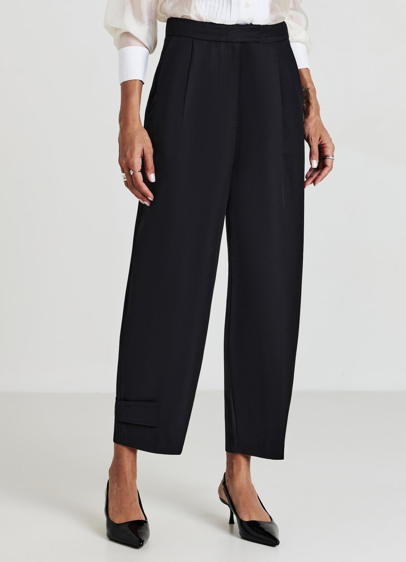 Pantalons noirs à coupe décontractée, avec des plis avant, une texture lisse et un ourlet à revers. Assortis à des talons noirs pointus.