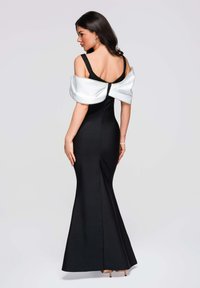 Robe noire à silhouette ajustée avec une évasement sirène. Comprend un surplis blanc en satin semblable à une cape et une fermeture éclair à l'arrière. Texture lisse.