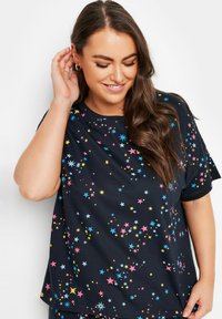 Svart t-shirt i mjukt material med ett spritt stjärnmönster i rosa, blå och gula nyanser. Kortsleeve, avslappnad passform.