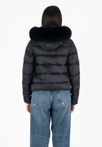 Giacca a vento nera con cappuccio foderato in pelliccia, caratterizzata da un design trapuntato e una silhouette aderente. Indossata con jeans blu a vita alta.
