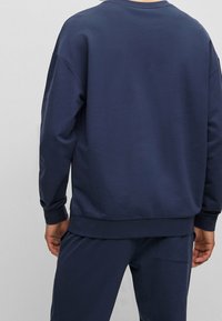 Sudadera azul marino hecha de un tejido suave, con cuello redondo, puños acanalados y un corte holgado. La vista trasera muestra simplicidad y comodidad.