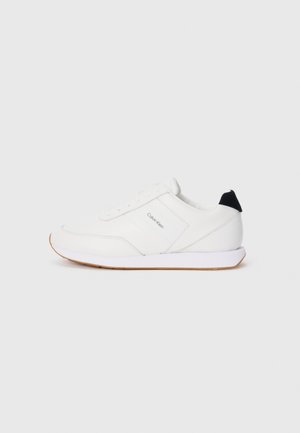 Witte sneaker met een gladde textuur, met een minimalistisch ontwerp, subtiele branding aan de zijkant en een contrasterende zwarte hielaccent.