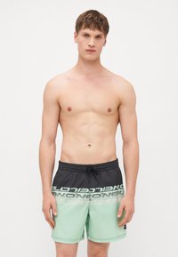 Shorts de bain pour hommes avec un design bicolore. Partie supérieure noire avec imprimé logo blanc, partie inférieure en vert menthe. Comprend une taille ajustable avec cordon.