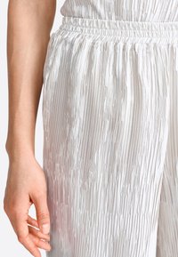 Pantaloni bianchi a pieghe con un elastico in vita, caratterizzati da una texture liscia e lucida. Il tessuto presenta un design stropicciato e linee verticali.