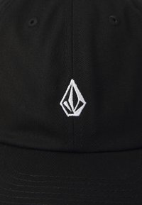 Căciulă neagră confecționată dintr-un material texturat, având un logo brodat alb în forma geometrică pe panoul din față. Design structurat, curea ajustabilă.