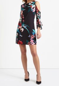 Blommönstrad klänning med svart bakgrund, har kallaxel-design, långa genomskinliga ärmar och en figursydd silhuett.