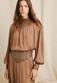 Abito marrone a pieghe con maniche lunghe, caratterizzato da una cintura dettagliata e decorata e un colletto con motivo. Texture liscia, design elegante.
