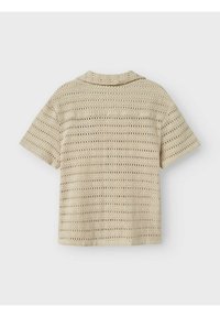 Chemise en crochet beige à manches courtes, dotée d'un design en maille ajourée et d'un col. La texture est lâche et aérée, permettant de voir à travers le tissu.