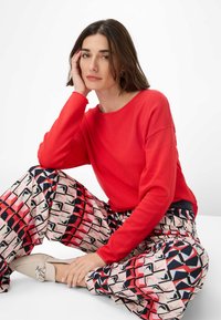 Red long-sleeve shirt, wide patterned pants in pink, red, and black geometric design, and beige flats with a decorative buckle.