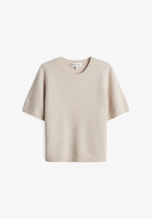 Pull beige à manches courtes fabriqué en matériau doux et texturé. Il présente un col rond et une coupe décontractée. Étiquette visible à l'intérieur du col.