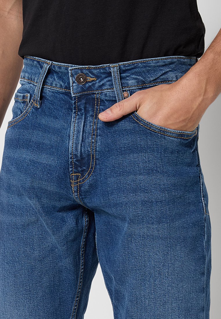 Blaue Denim-Jeans mit geradem Schnitt, ausgestattet mit Vordertaschen, hellen Stitching-Akzenten und einem gebrandeten Taillenknopf.