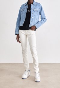 Chaqueta de mezclilla azul claro con botones en el frente, camiseta negra, jeans blancos ajustados y zapatillas blancas con detalles azules. Texturas suaves, estilo casual.