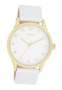 Montre analogique dorée avec un cadran blanc, des chiffres arabes et des aiguilles dorées. Elle dispose d'un bracelet en silicone blanc lisse et d'un design minimaliste.