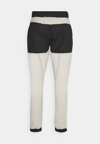 Tvåfärgade byxor med elastiskt midjeband. Svart övre del med krämfärgad nedre del. Har en slät textur och åtsittande mudd.