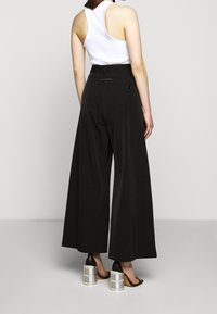 Pantalones de pierna ancha negros con cintura alta, que cuentan con un detalle de botón en la parte trasera. Combinados con una blusa blanca sin mangas y sandals de tacón alto únicas.