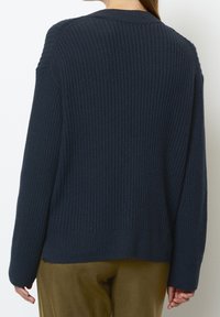 Pull en maille côtelée bleu marine avec un col rond. Présente une coupe décontractée, des épaules tombantes et des détails texturés sur toute la surface.