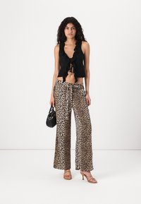 Schwarzes, ärmelloses Oberteil mit Rüschenrand, kombiniert mit weiten Leopard-Print-Hosen. Accessoires: kleine schwarze Handtasche und Riemchensandalen.